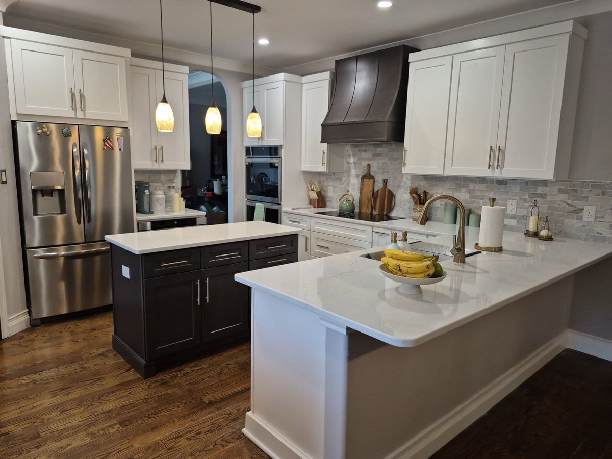 White kitchen with dark wood vent hood, marble backsplash and brass pulls