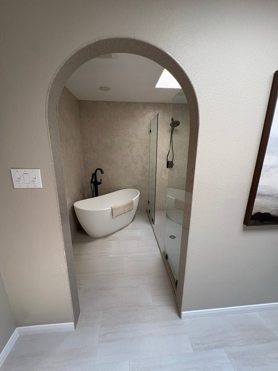 Arched entry view of white freestanding soaking tub with black floor faucet