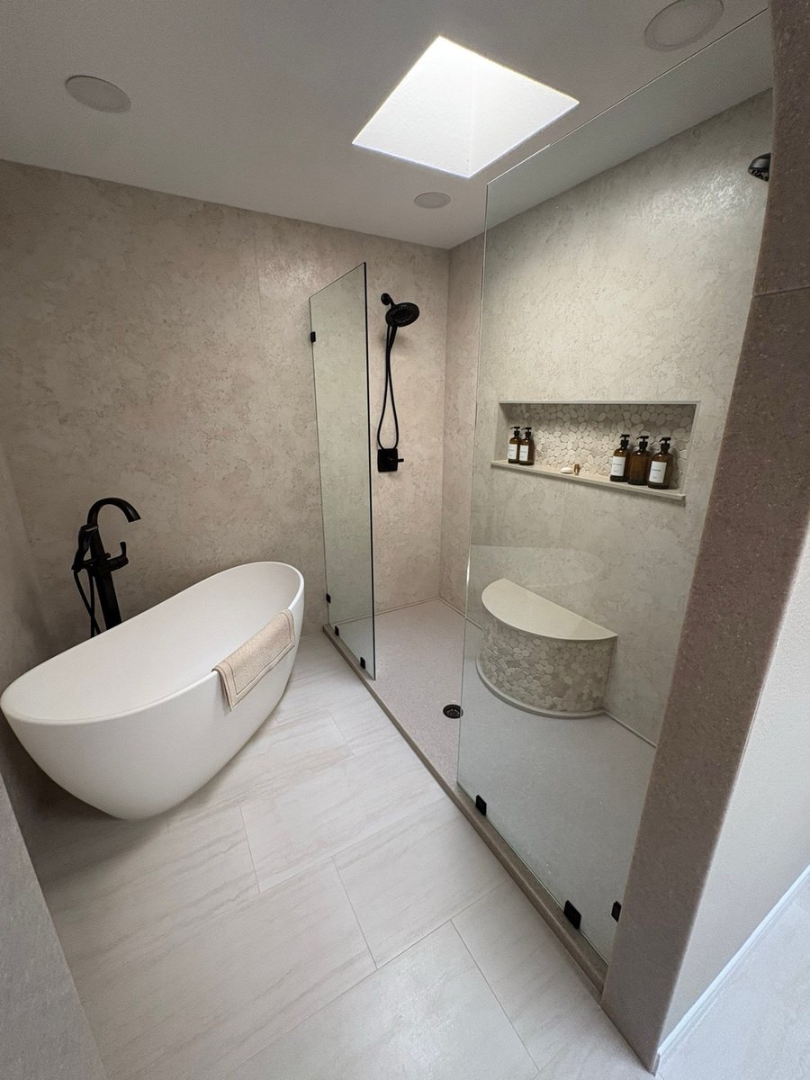 White freestanding tub beside glass shower with beige walls and curved bench