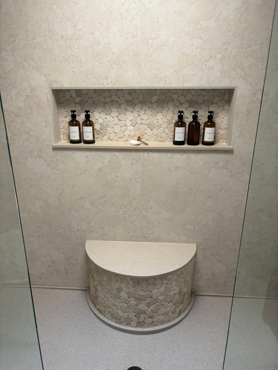 Recessed pebble tile niche above rounded shower bench in beige stone walls