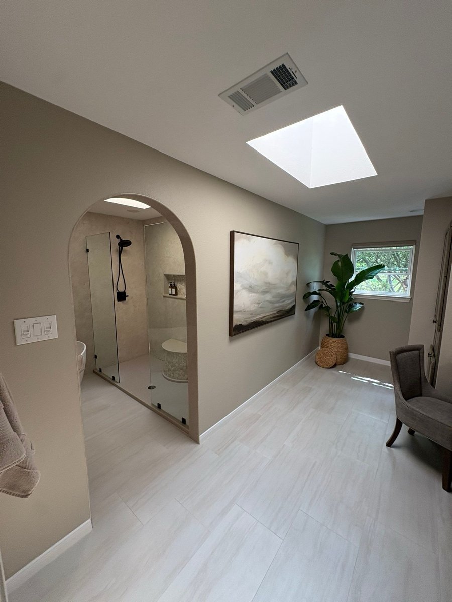 Spacious master bath with glass shower, landscape art and potted plant by window