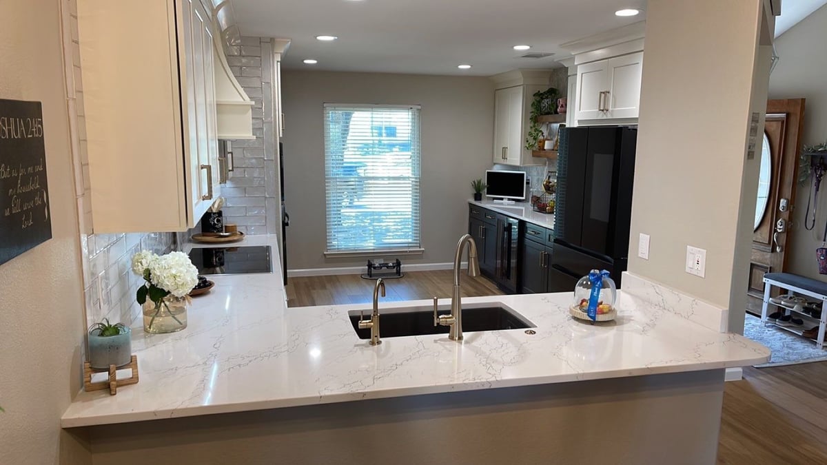 Galley kitchen view across quartz peninsula toward window and dark cabinets