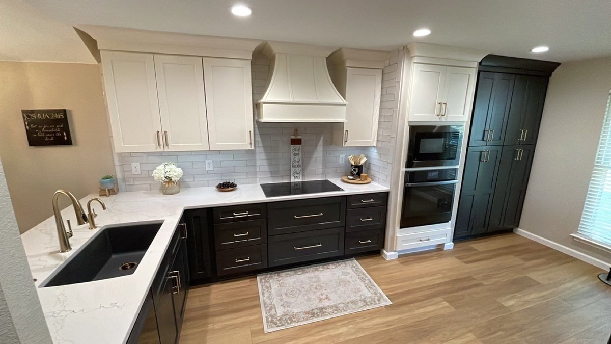 Kitchen with cream cabinets, dark lowers, white range hood and induction cooktop