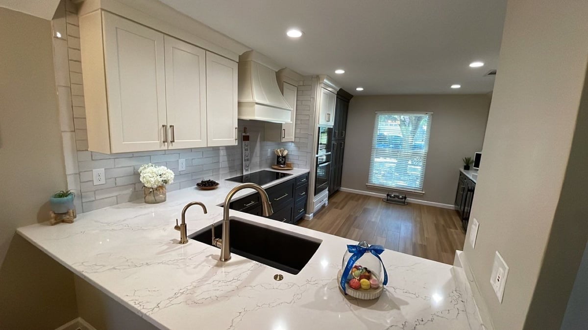Cream upper cabinets, dark base cabinets and white range hood over cooktop