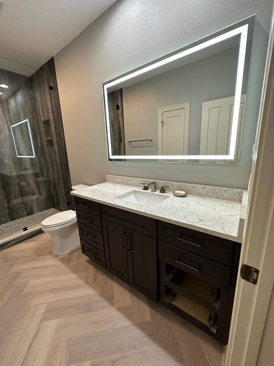Bathroom with dark vanity, lighted mirror and dark stone walk-in shower
