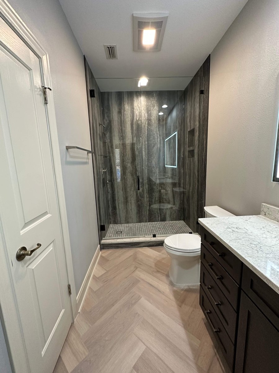 Narrow bathroom with glass shower in dramatic gray stone and herringbone floor