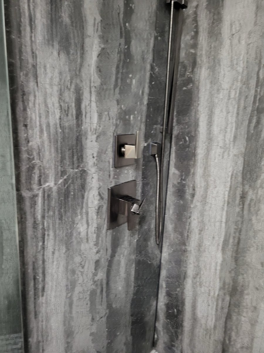 Black fixtures and handheld sprayer mounted on veined gray stone shower wall