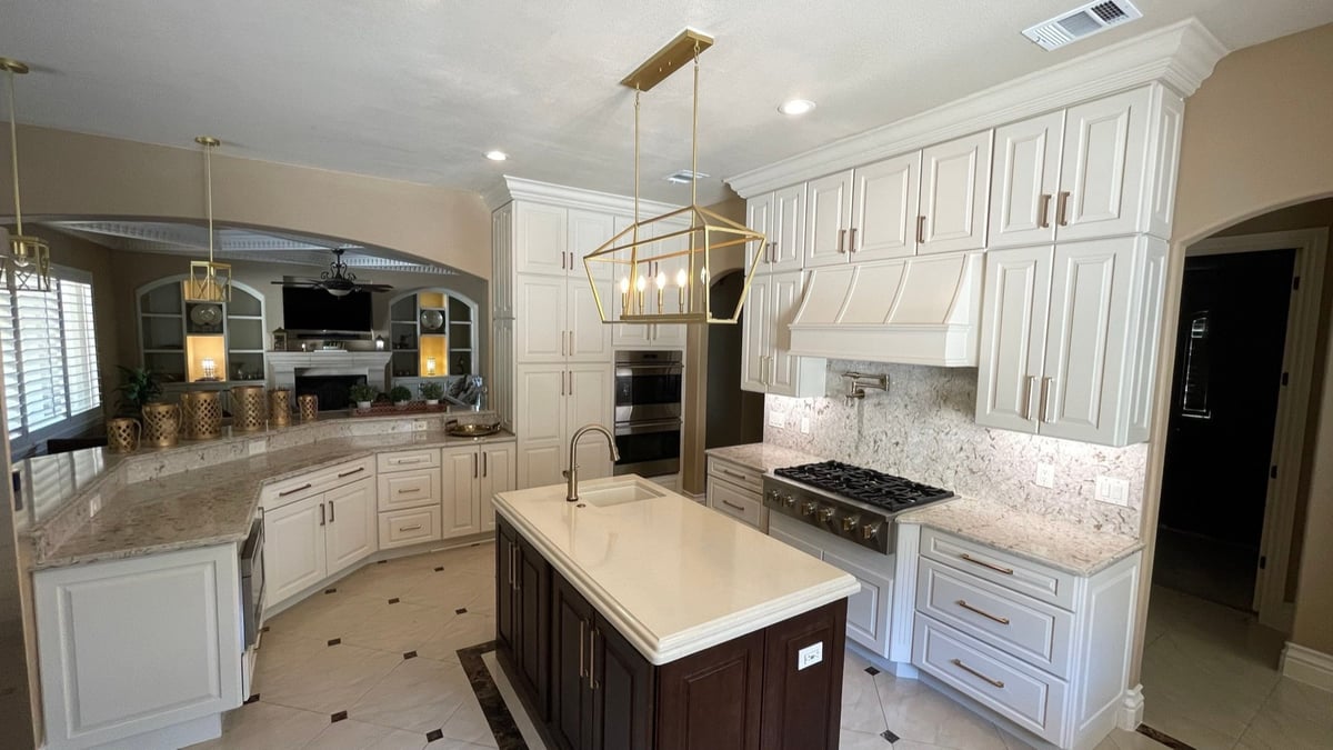 Wide cream kitchen with dark island, gas range, glass-front uppers, and brass pendant