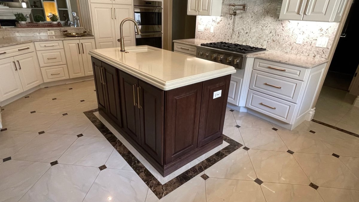 Dark wood island with quartz top and gold faucet beside gas range and white cabinets
