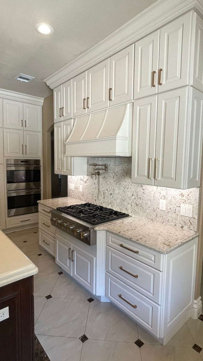 White cabinets and range hood over gas cooktop with granite counters and patterned floor