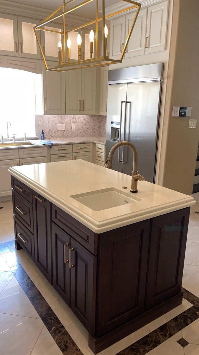 Dark island with gold faucet, stainless built-in fridge, and brass lantern pendant