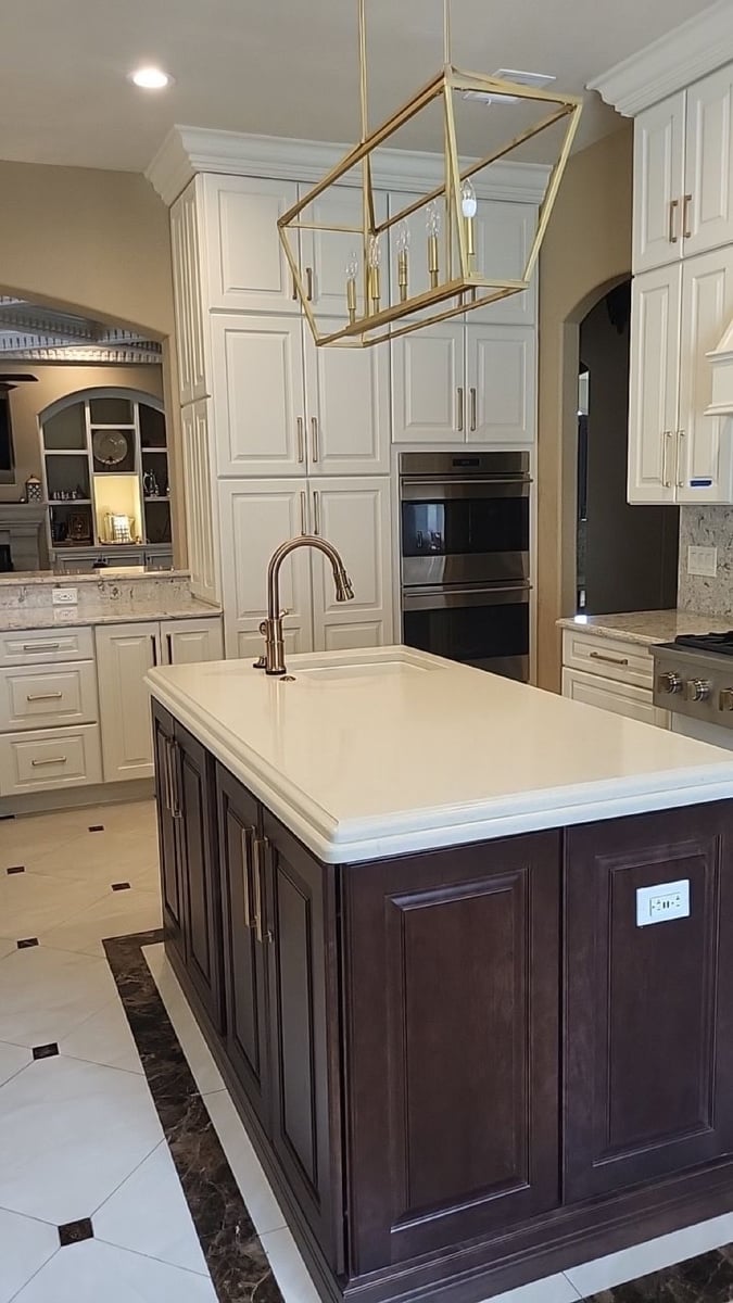 Dark wood island with gold faucet under brass lantern pendant and white cabinets