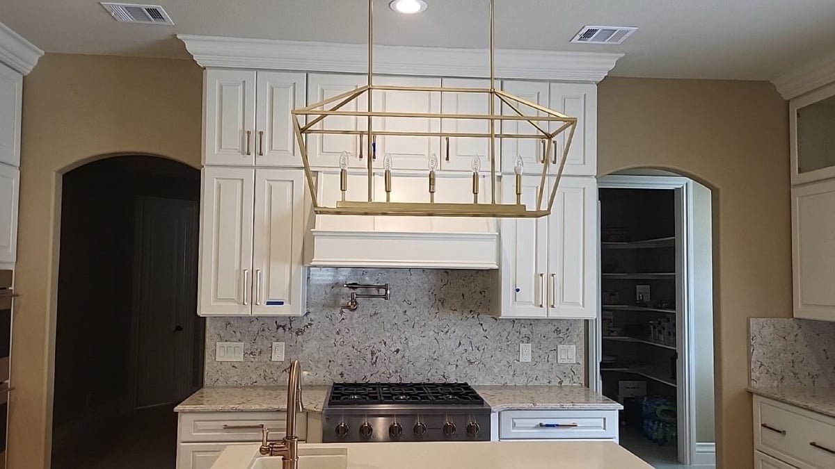 White cabinets and range hood over gas cooktop with granite backsplash and pantry