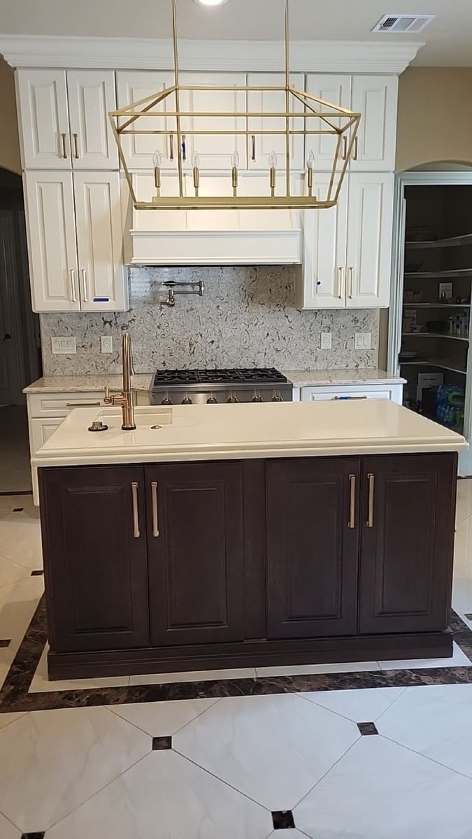 Dark island facing gas range below brass linear pendant and white cabinets