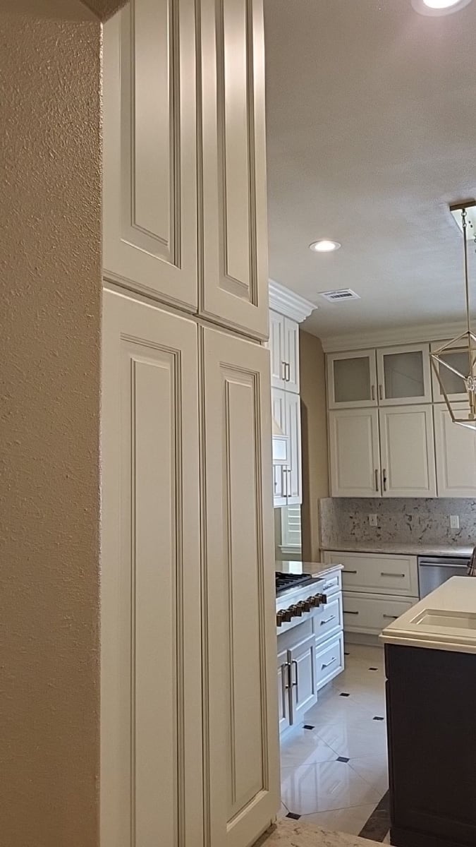 Tall cream cabinets in foreground with view toward range and dark island