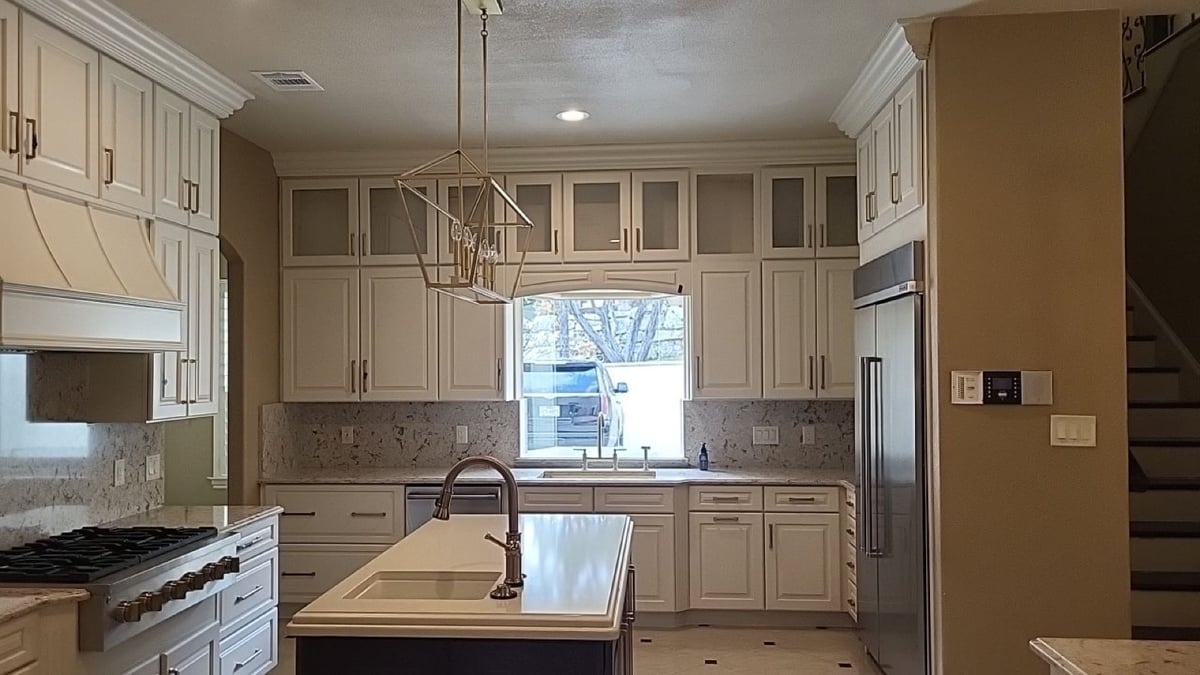 White kitchen with arched window over sink, stainless fridge, and gas cooktop