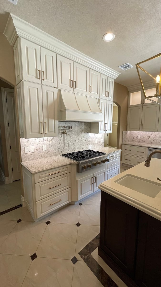 Cream cabinets and range hood over gas cooktop with granite counters and tile floor