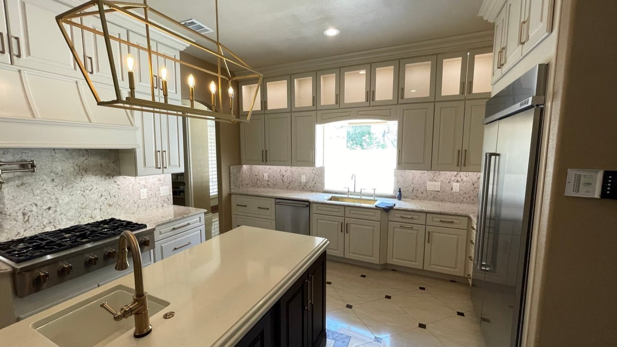Cream kitchen with gas range, dark island, stainless fridge, and brass pendant