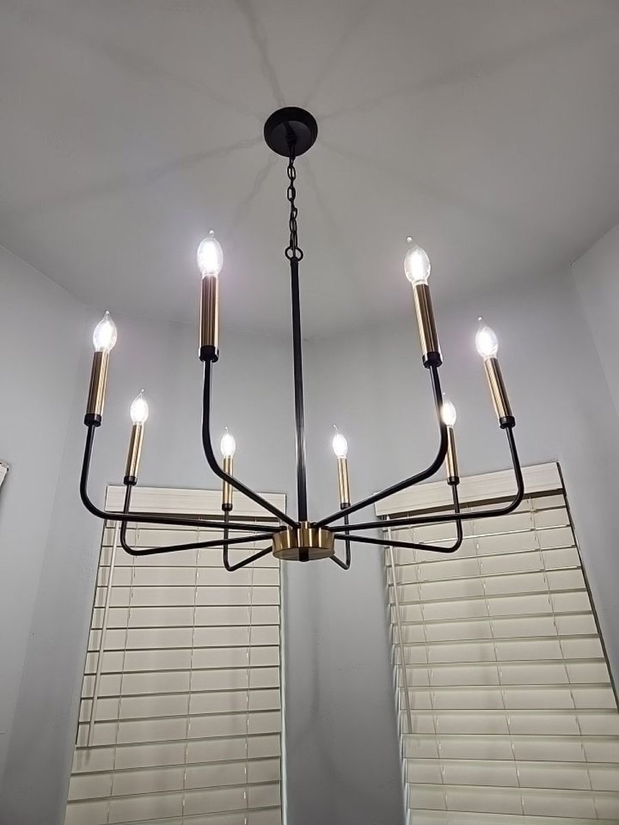 Black and brass eight-light candle chandelier above white wood-blind windows