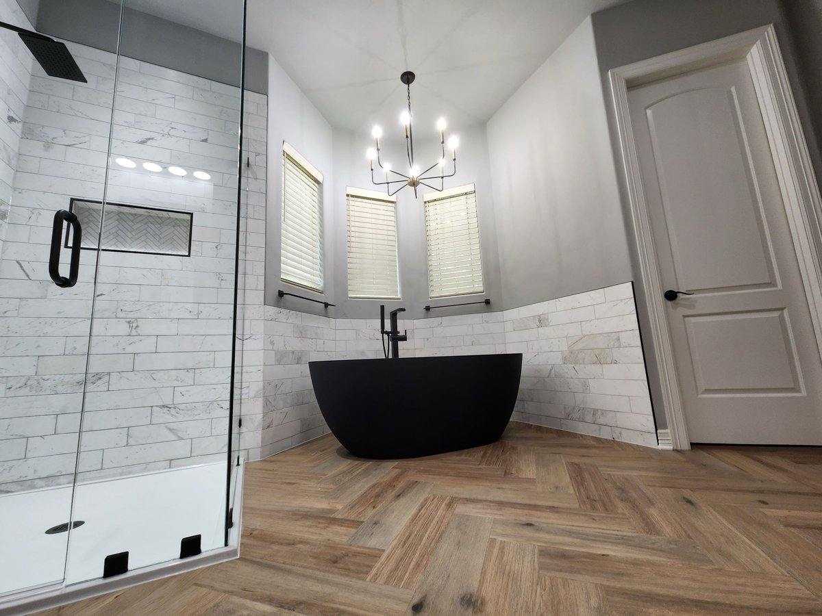 Matte black soaking tub against white-and-marble tiled wainscot wall
