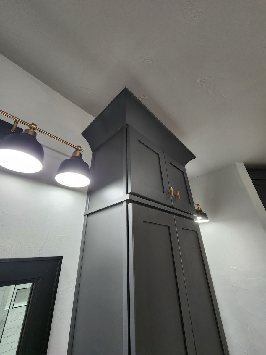 Charcoal cabinet crown molding lit by brass and navy vanity sconces