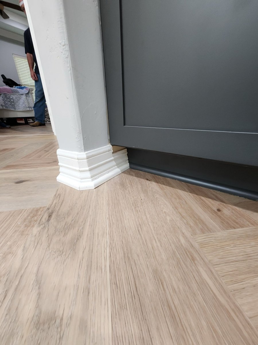 Detail of herringbone wood floor meeting white column and charcoal cabinet base