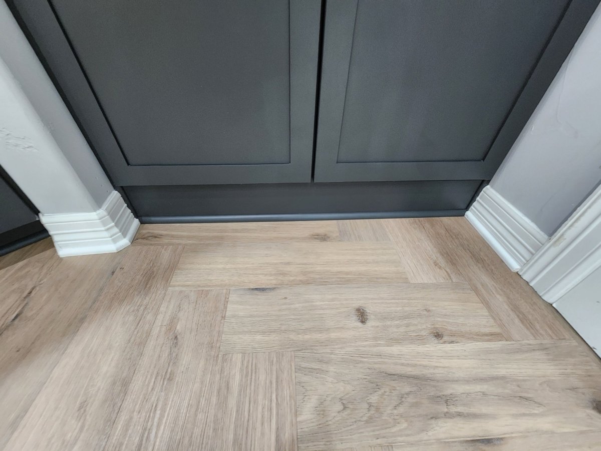 Charcoal cabinet toe-kick and white trim over herringbone wood floor