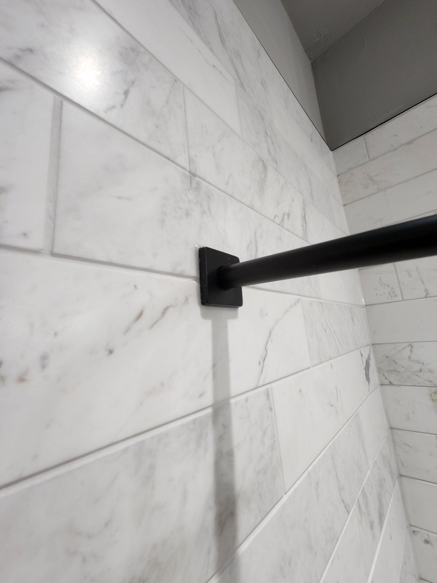 Black towel bar mounted on marble subway-tiled shower wall