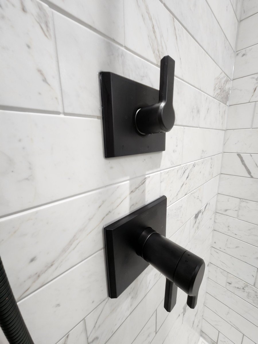 Matte black Delta shower handle and tub spout on marble tile