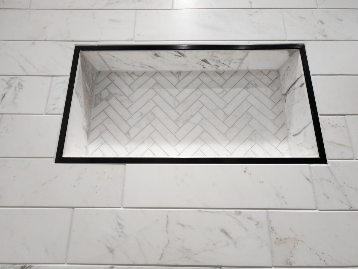 Recessed shower niche with black trim and herringbone marble mosaic back