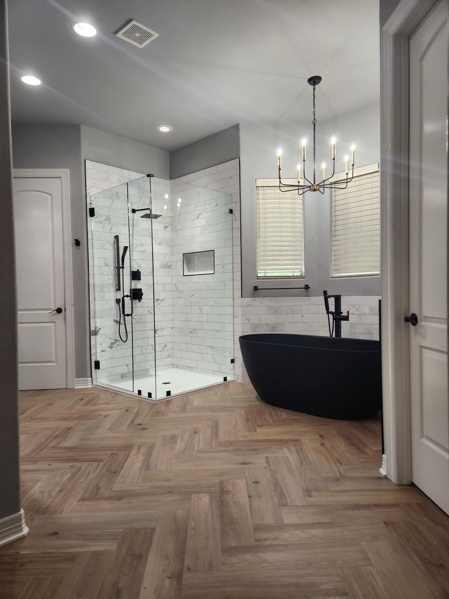 Remodeled master bath with glass corner shower, black soaking tub and herringbone wood floor
