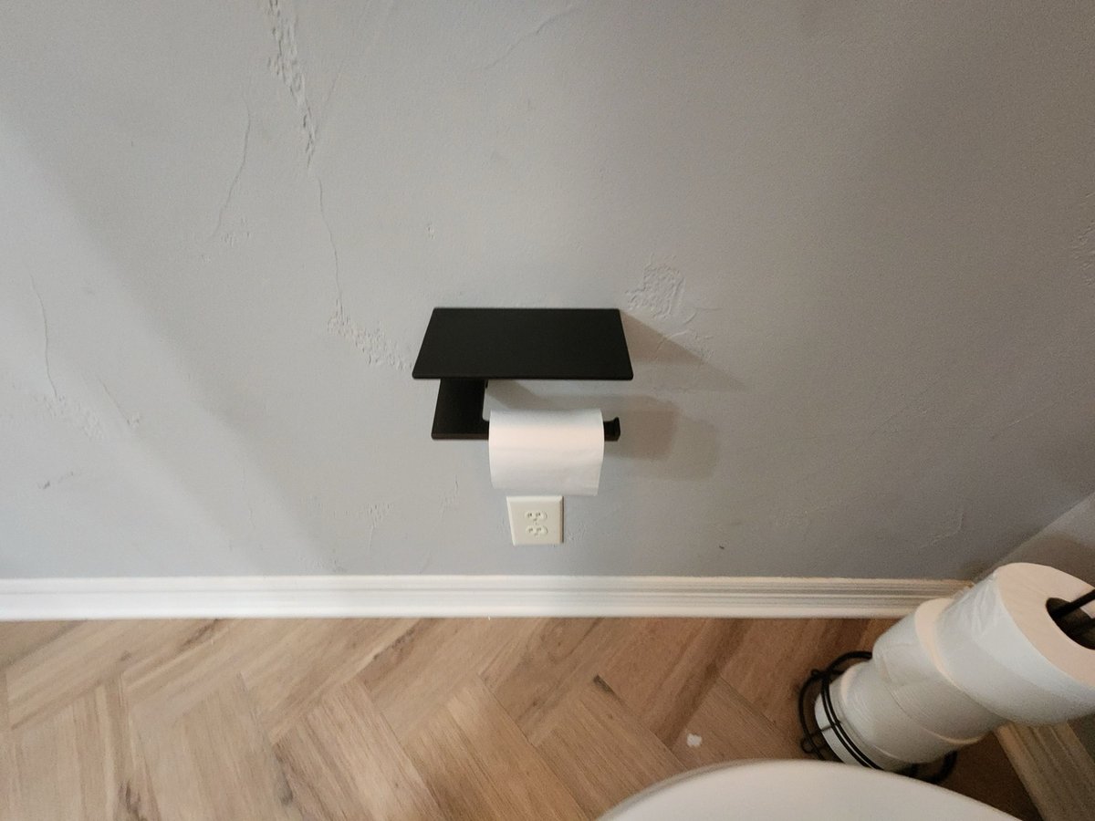 Black shelf toilet paper holder on gray wall above herringbone floor