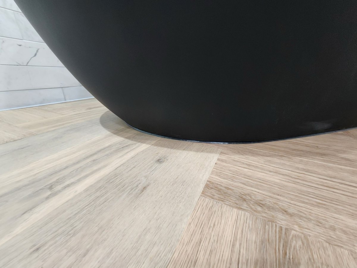 Base of matte black freestanding tub on herringbone wood-look floor