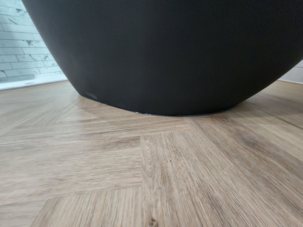 Curved base of black soaking tub against marble tile and wood floor