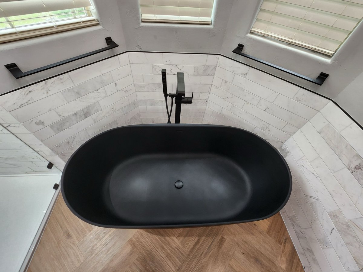 Overhead view of black oval tub with floor-mounted faucet and marble surround