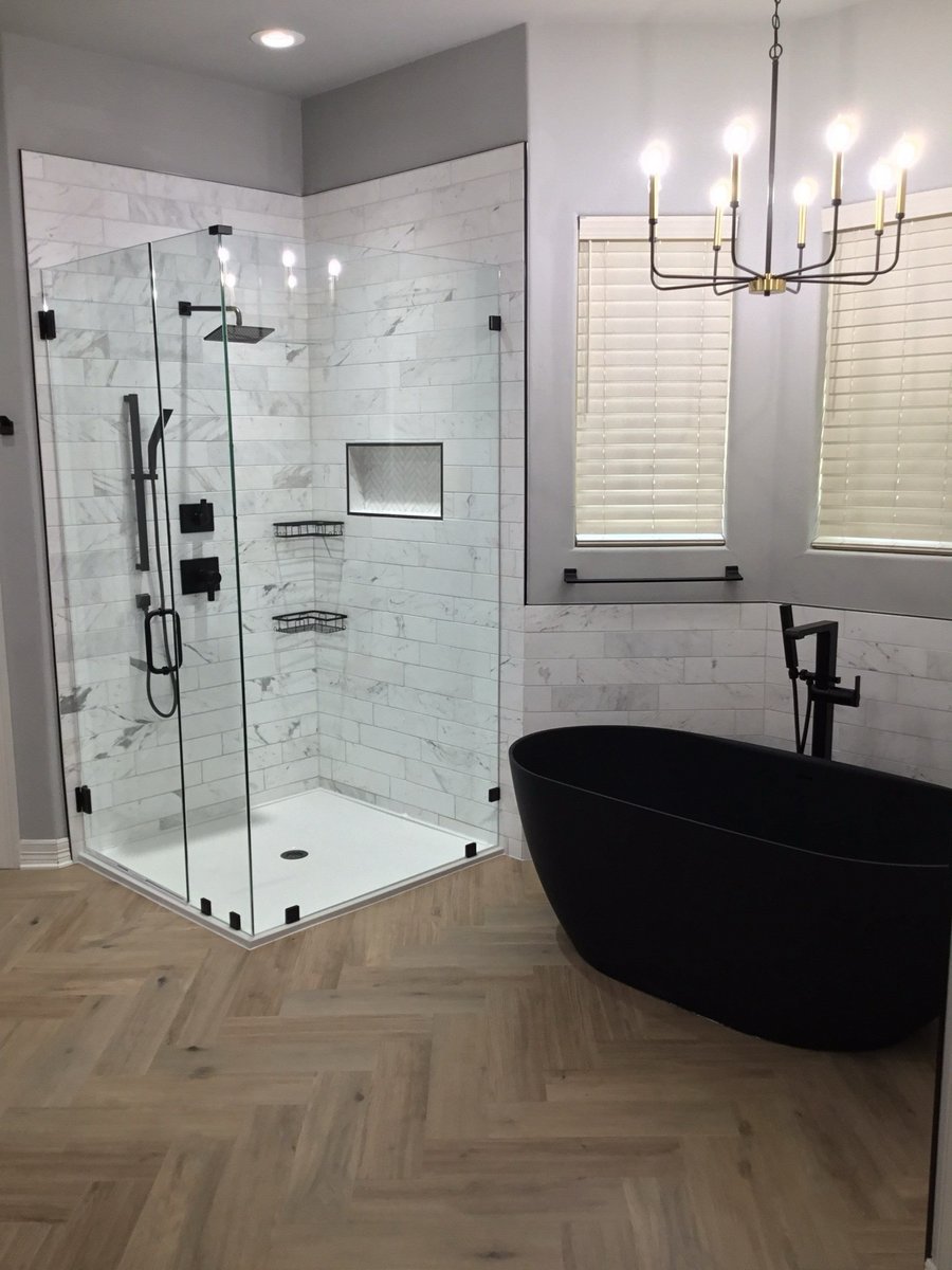 Corner glass shower and black freestanding tub by blind windows