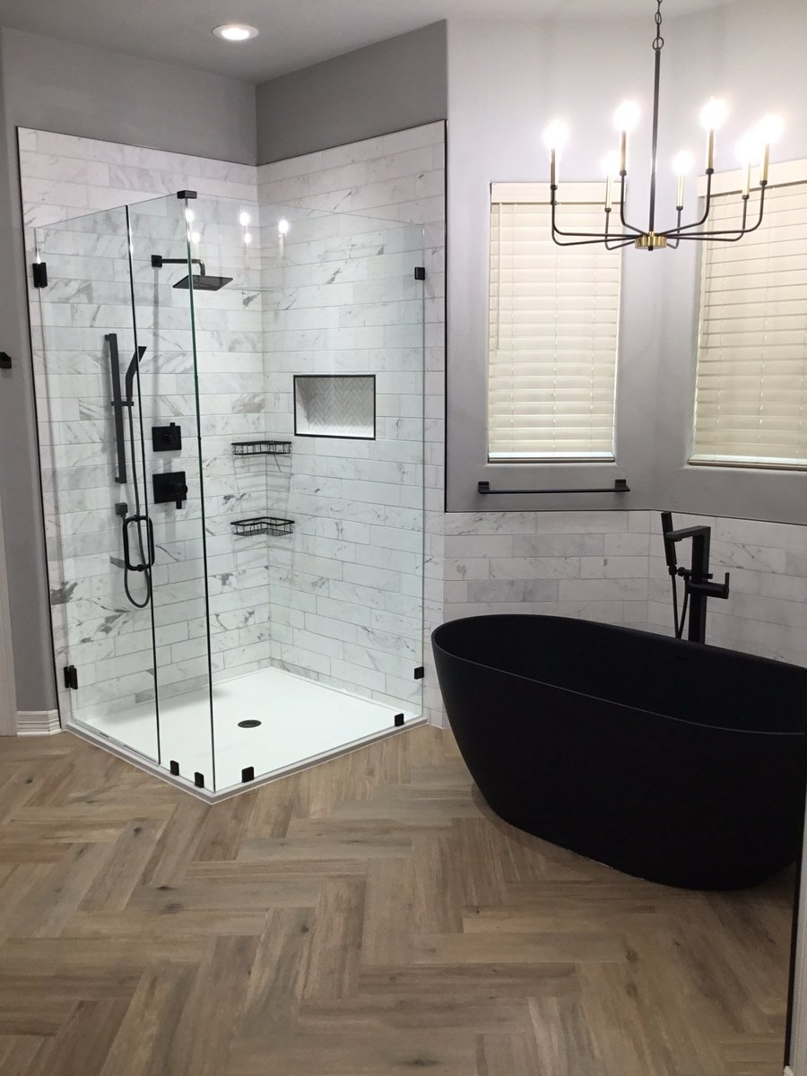 Frameless glass shower with marble walls beside matte black soaking tub