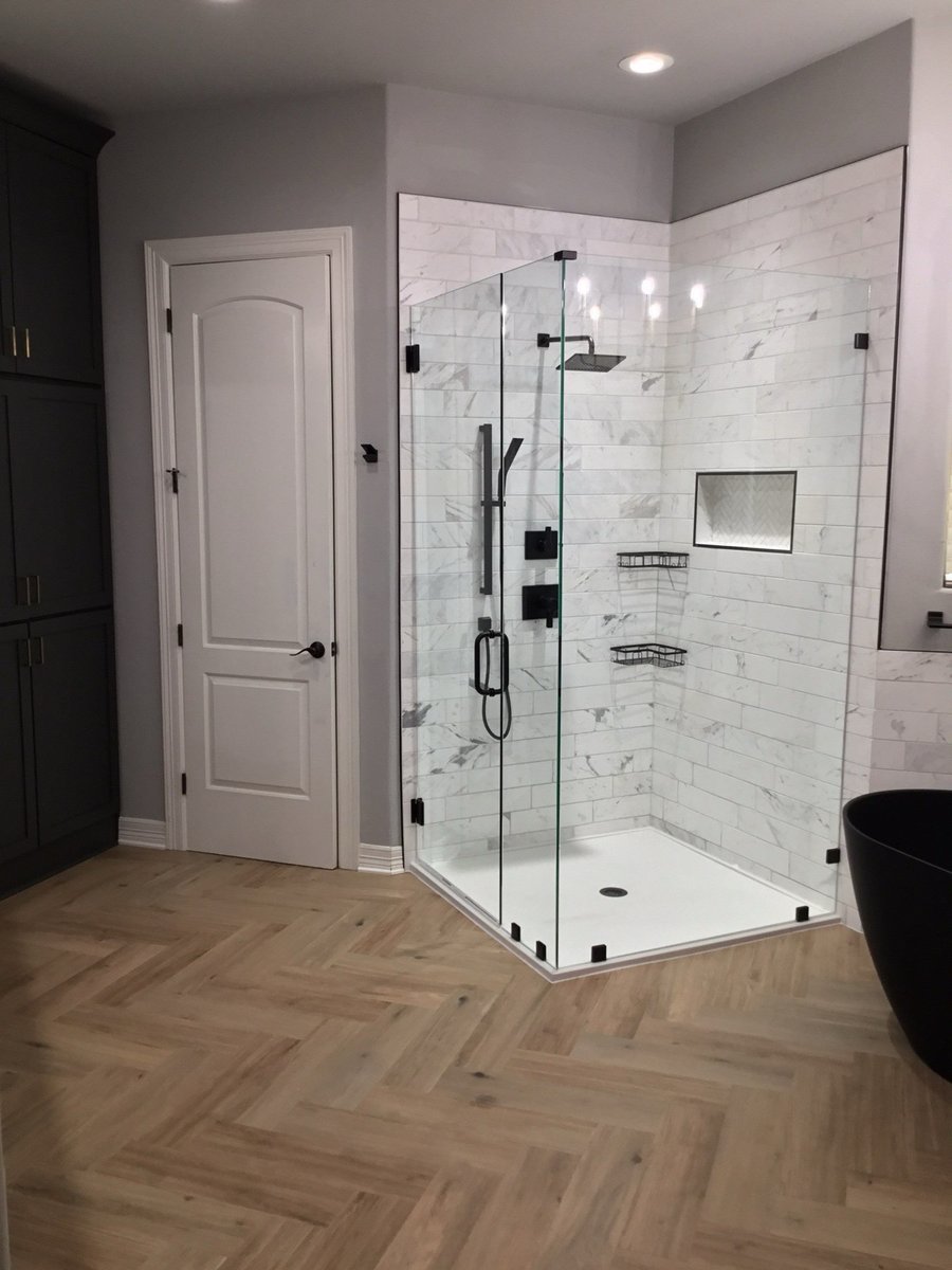 Glass corner shower next to white door, charcoal cabinets and black tub