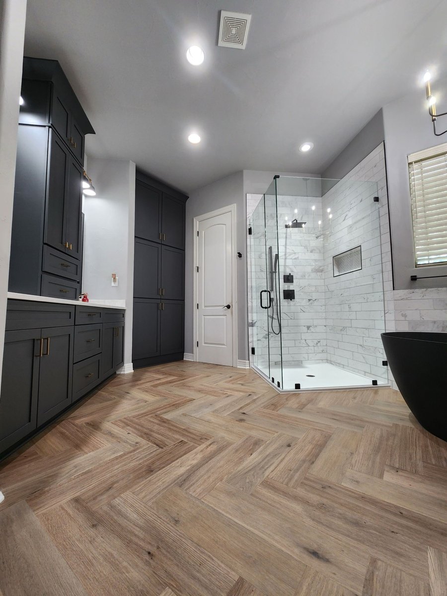 Dark gray double vanity and tall linen cabinets beside marble-tiled glass shower