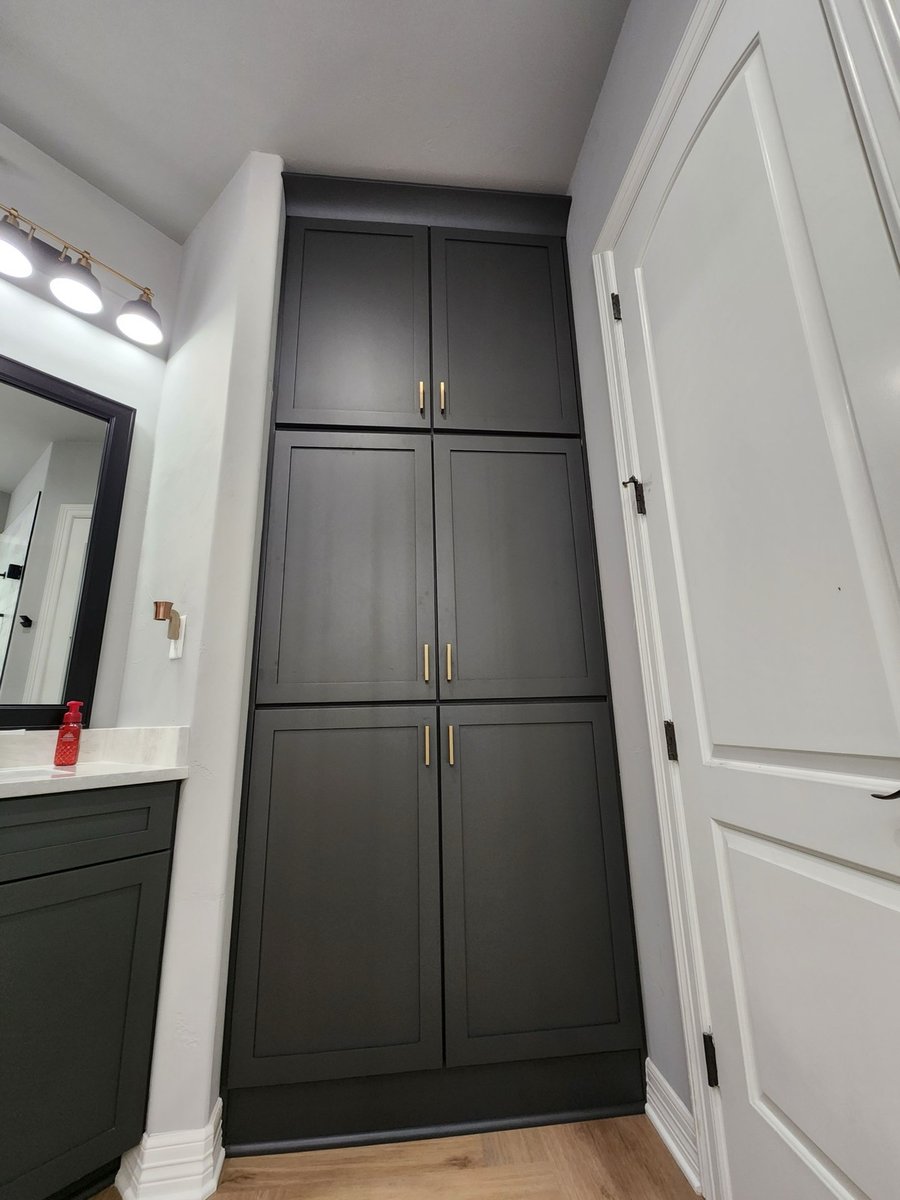 Floor-to-ceiling charcoal linen cabinet with brass pulls next to white door