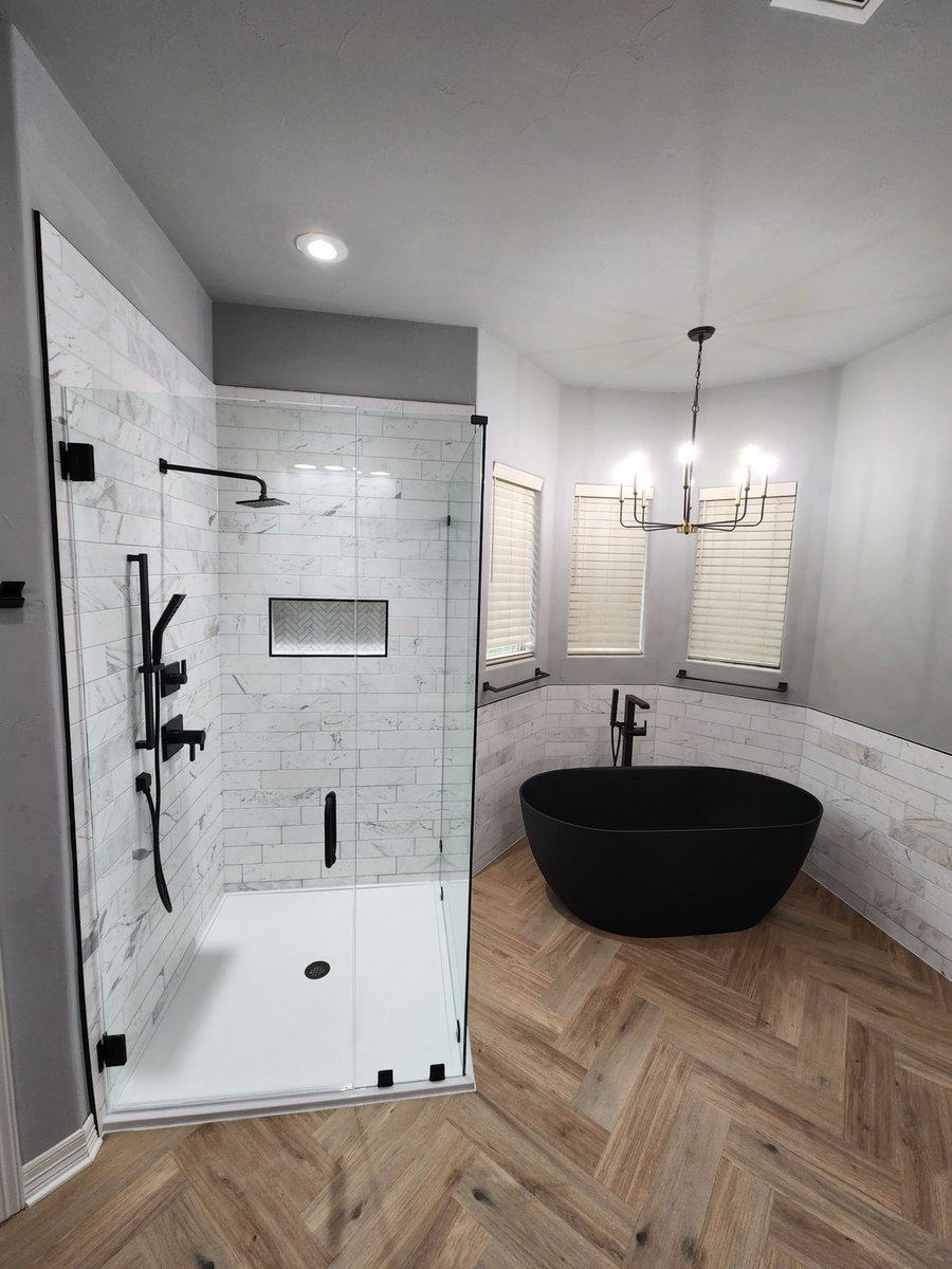 Marble subway-tiled walk-in shower and matte black freestanding tub under chandelier