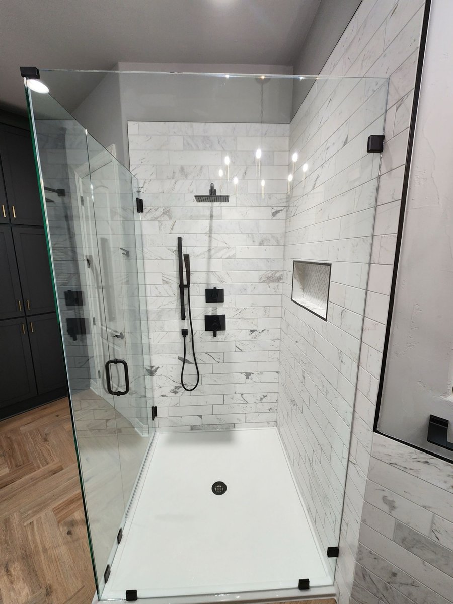 Frameless glass corner shower with marble tile, black rainfall head and herringbone niche