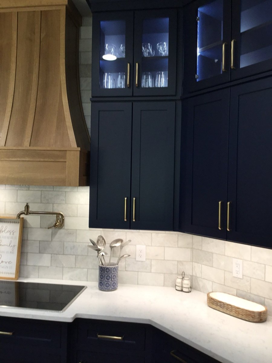 Navy cabinets with wood hood, white subway tile and brass bridge faucet at island