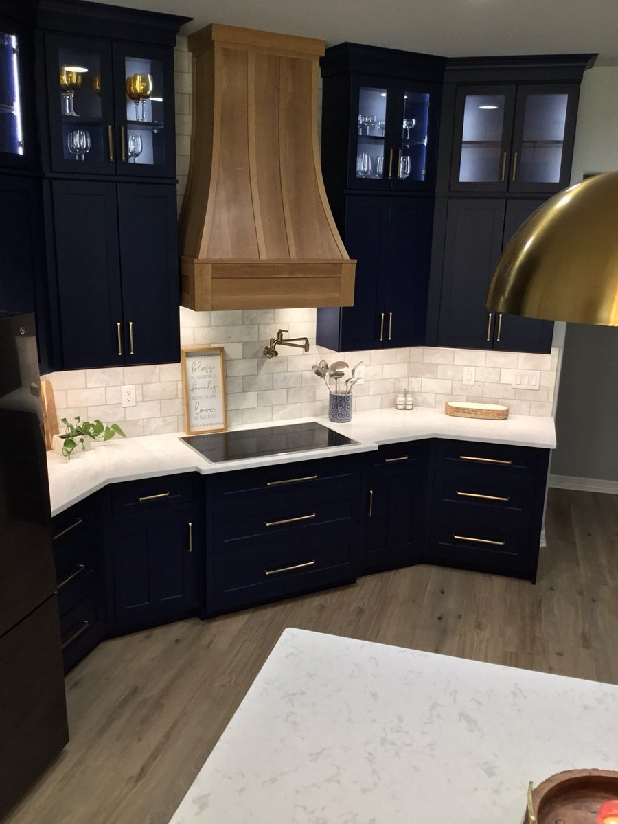 Brass bridge faucet on white quartz island with navy cabinets and wood hood behind