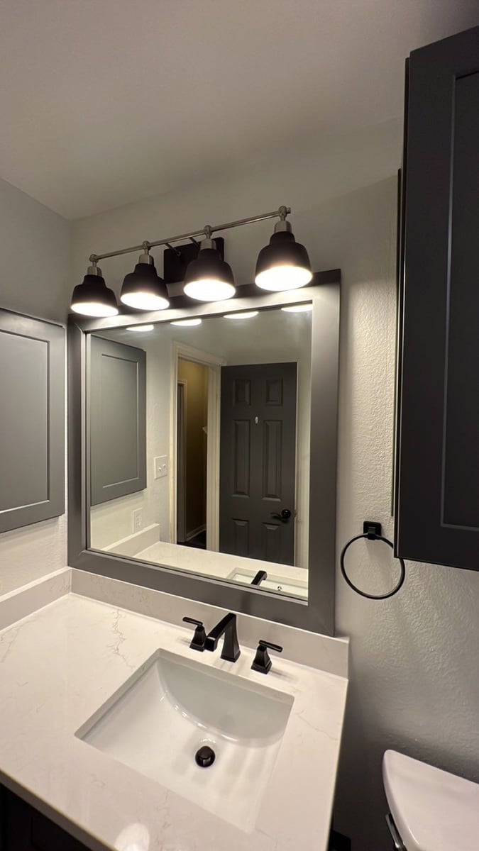 Bathroom vanity with white quartz top, black faucet, and large gray-framed mirror