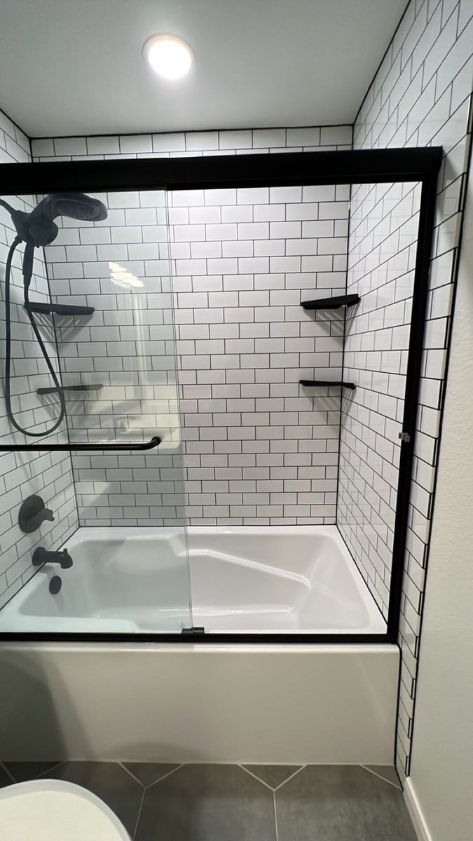 Tub-shower combo with white subway tile, black grout, and black trim glass door