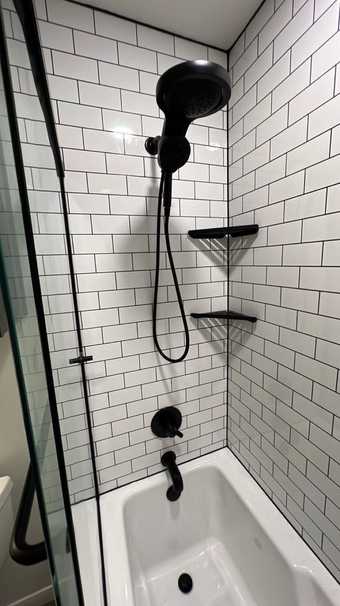 White subway tile shower with black handheld fixture and corner shelves