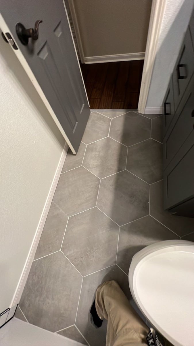 Gray hexagon tile bathroom floor leading to dark wood hallway