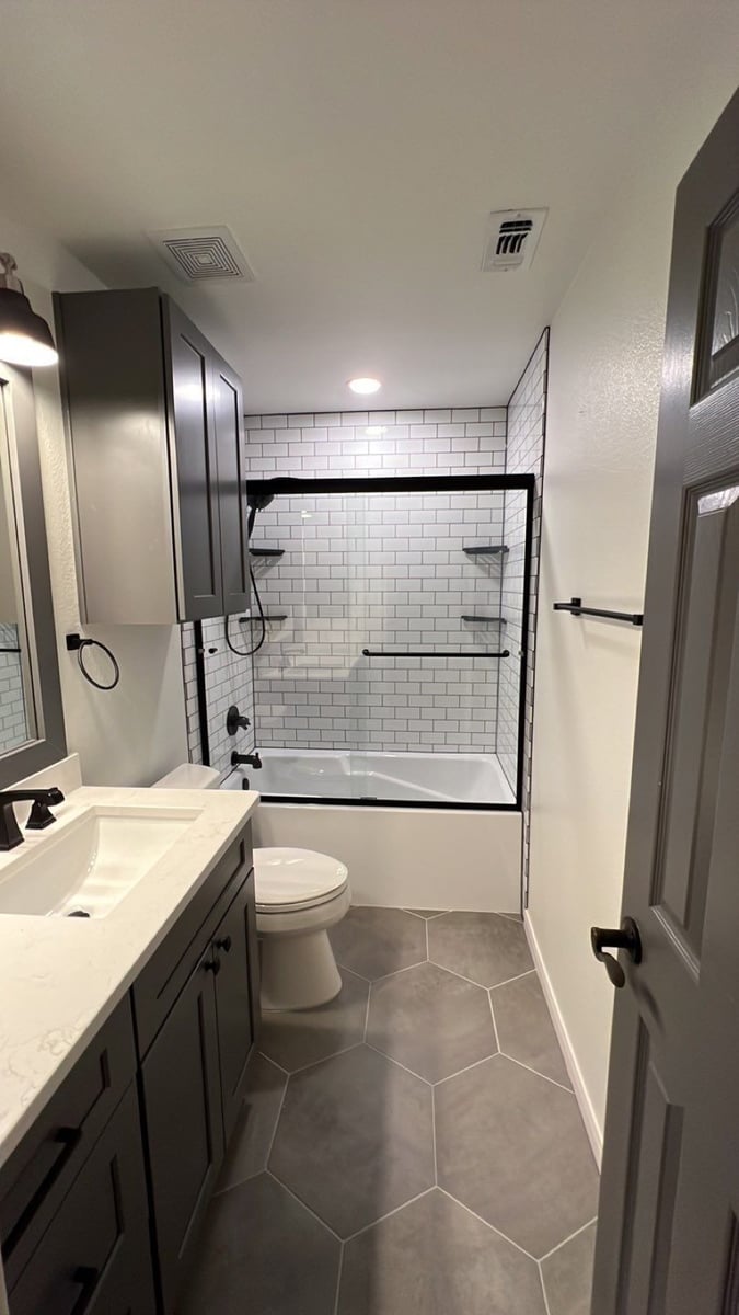 Remodeled bath with gray vanity, subway-tiled tub surround, and hexagon tile floor