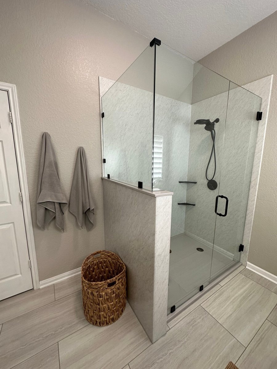 Remodeled walk-in shower with frameless glass, marble walls, and black fixtures